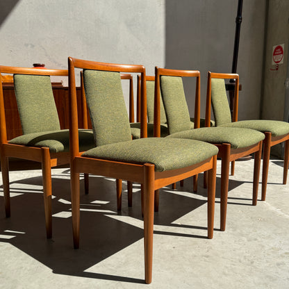 A set of six fully restored Parker T-Back Number 88 dining chairs in forest green upholstery is arranged in a row on a concrete floor, sunlight streaming against a plain, light-colored wall.