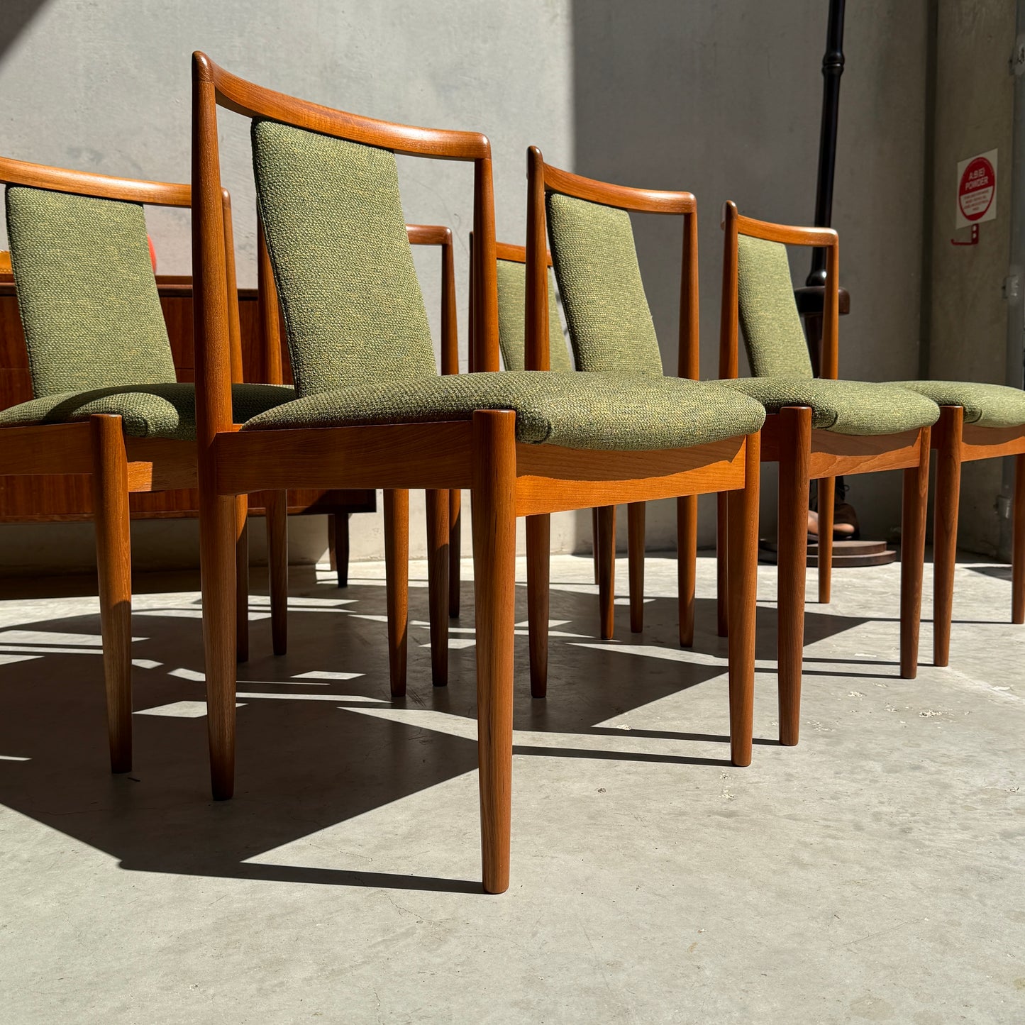 Six fully restored Parker T-Back Number 88 dining chairs in forest green upholstery are arranged on a concrete floor, creating a striking mid-century modern accent in this minimalist indoor space.