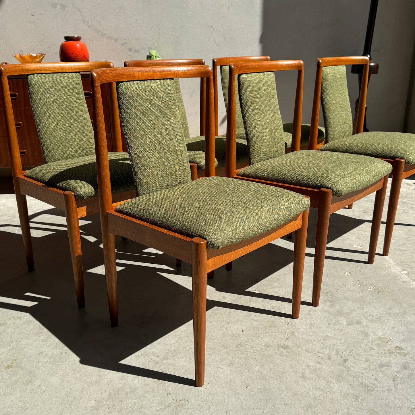 Six fully restored Parker T-Back Number 88 mid-century dining chairs in forest green upholstery are arranged outdoors in sunlight, highlighting their elegant wooden frames and tapered legs.