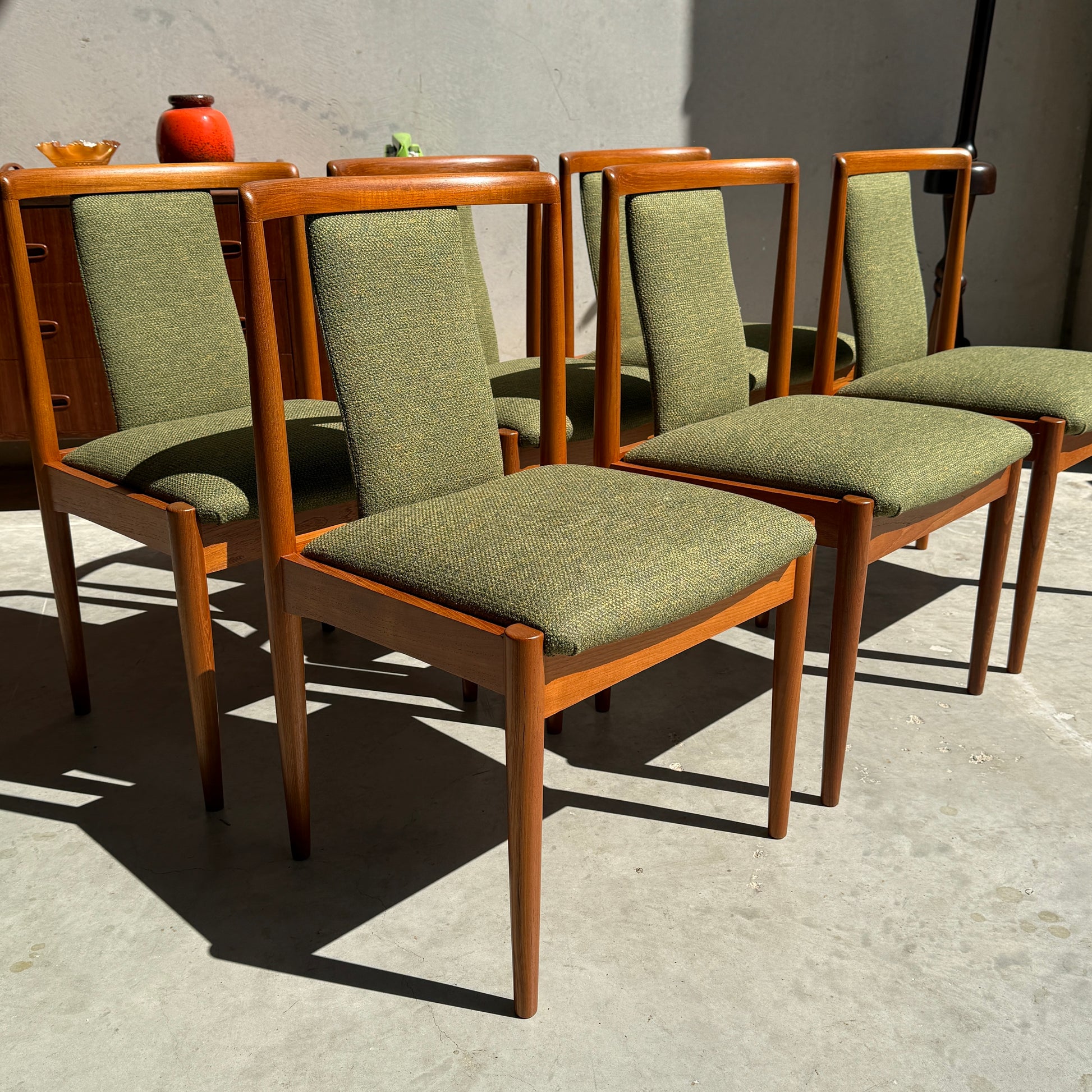 Six fully restored Parker T-Back Number 88 mid-century dining chairs in forest green upholstery are arranged outdoors in sunlight, highlighting their elegant wooden frames and tapered legs.