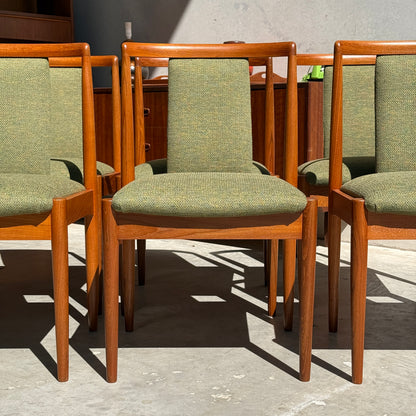 Six fully restored Parker T-Back Number 88 dining chairs with forest green upholstery are arranged in a row on a sunlit concrete floor, with a Parker Furniture sideboard visible in the background.