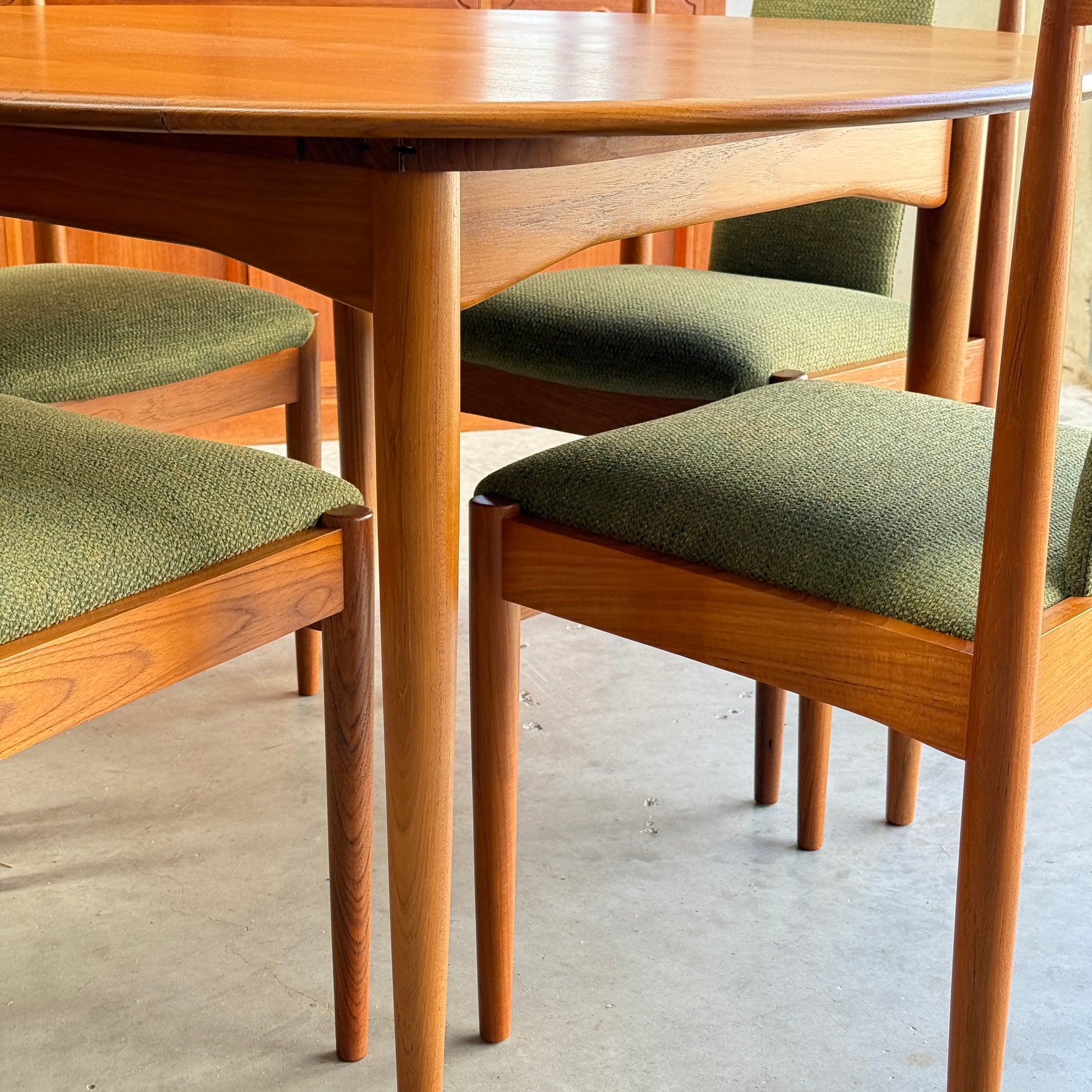 Set of six fully restored Parker T-Back Number 88 dining chairs in forest green, featuring upholstered seats and angled wooden legs, complementing a mid-century modern wooden dining table on a concrete floor.
