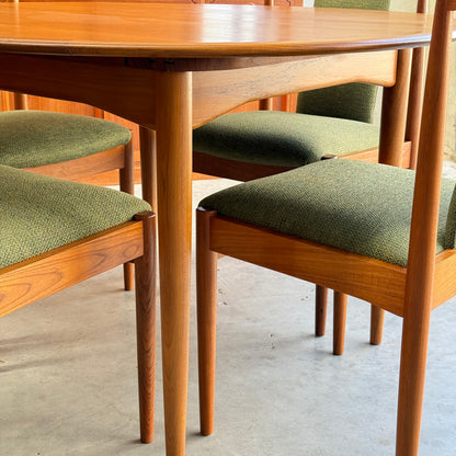 Set of six fully restored Parker T-Back Number 88 dining chairs in forest green, featuring upholstered seats and angled wooden legs, complementing a mid-century modern wooden dining table on a concrete floor.