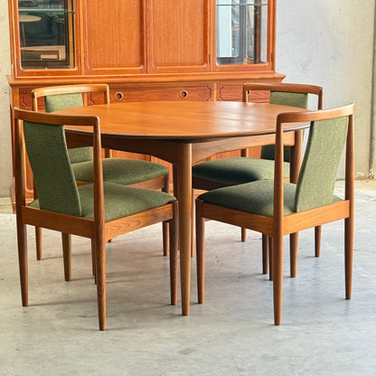 A round wooden dining table is paired with a set of six fully restored Parker T-Back Number 88 dining chairs in forest green, arranged before a wooden cabinet with glass doors and drawers for classic mid-century modern appeal.