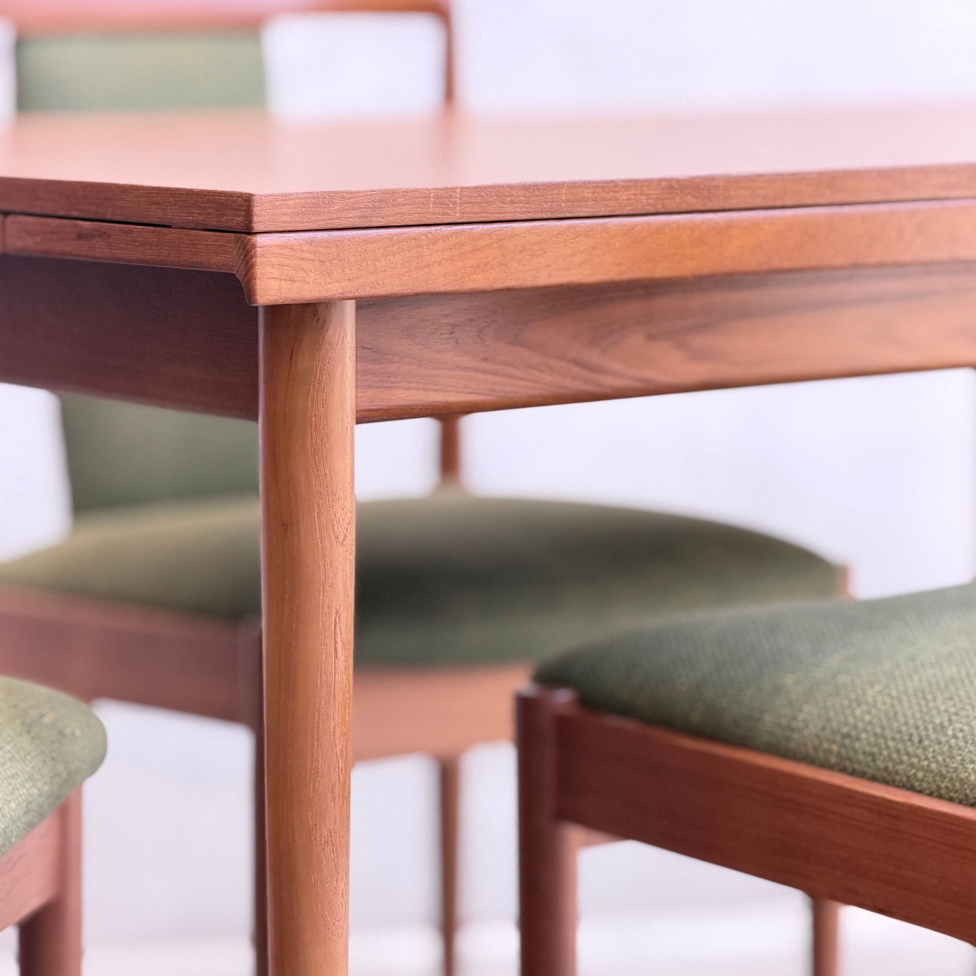 Close-up of the Fully Restored Parker Dining Suite 5 Piece - Forest Green by Rediscover, featuring a Scandinavian-inspired wooden table with rounded edges and matching chairs with green upholstery, set against a softly blurred background.