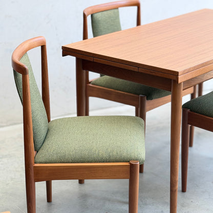 The Fully Restored Parker Dining Suite 5 Piece - Forest Green (Rediscover) features a Scandinavian-inspired wooden dining table and matching chairs with green upholstered seats and backrests, set on a light floor against a plain, light wall.