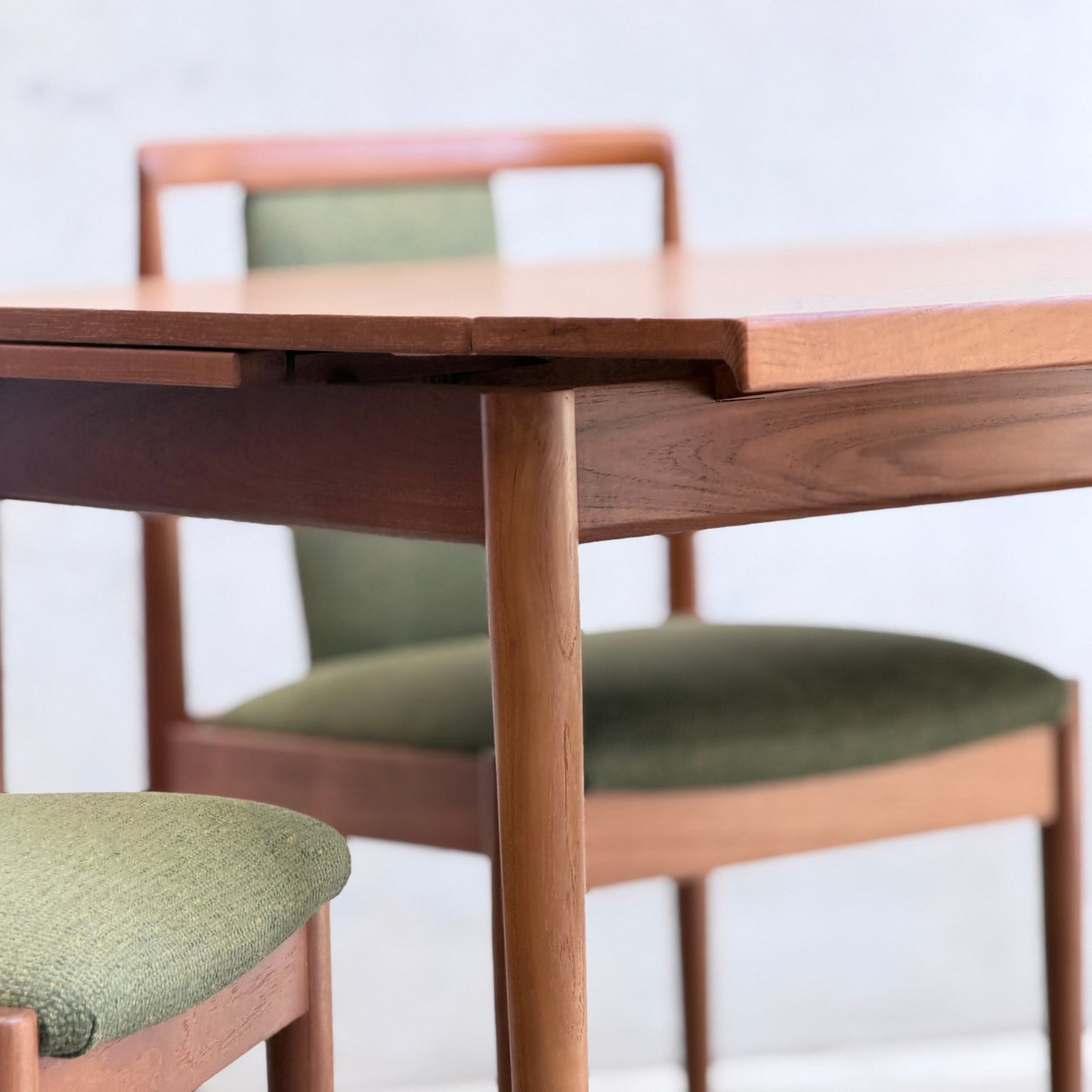 A close-up of the Fully Restored Parker Dining Suite 5 Piece - Forest Green (Rediscover) showcases its Scandinavian-inspired wooden table and two matching chairs with green upholstered seats and backs against a light, neutral background.