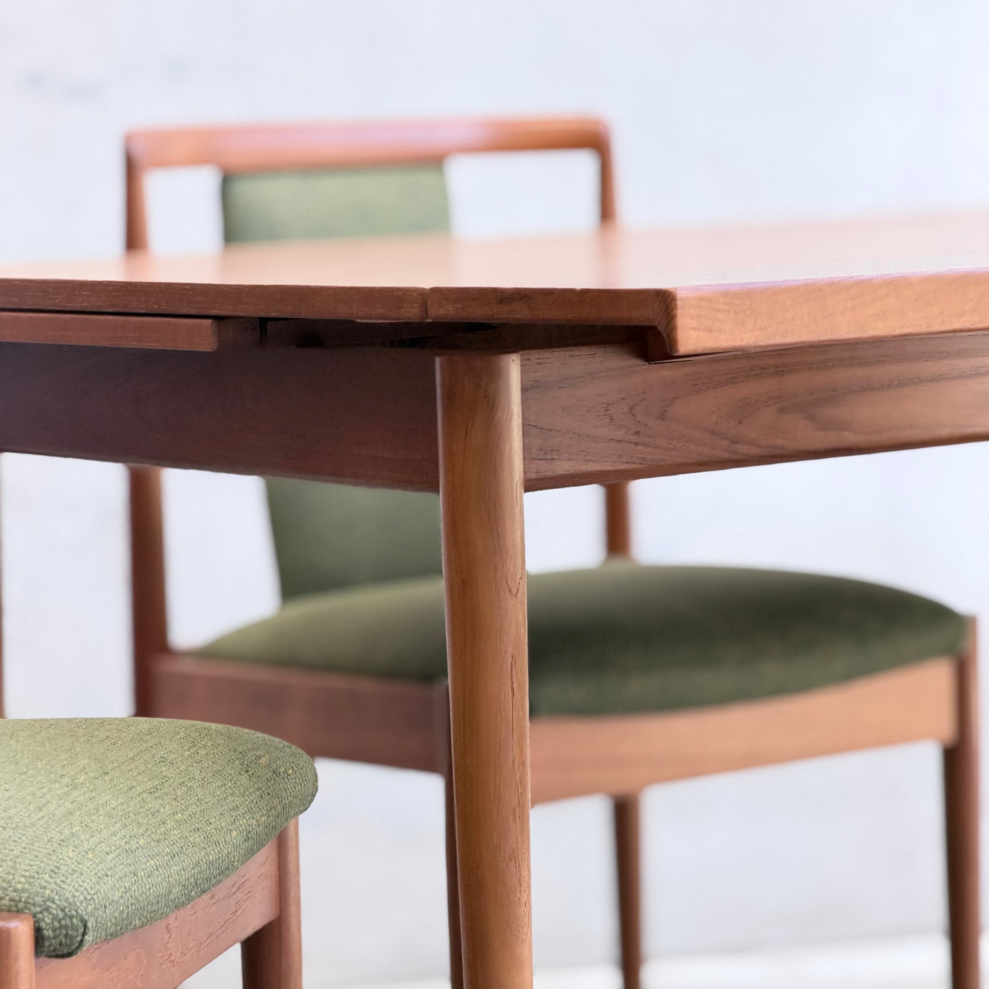 A close-up of the Fully Restored Parker Dining Suite 5 Piece - Forest Green (Rediscover) showcases its Scandinavian-inspired wooden table and two matching chairs with green upholstered seats and backs against a light, neutral background.