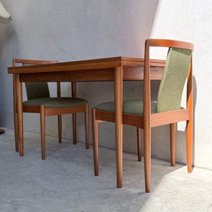A set of four fully restored Parker T-Back Number 88 dining chairs in forest green (Rediscover) is arranged by a matching wooden table in a minimalist, sunlit room with a concrete floor and light gray wall.