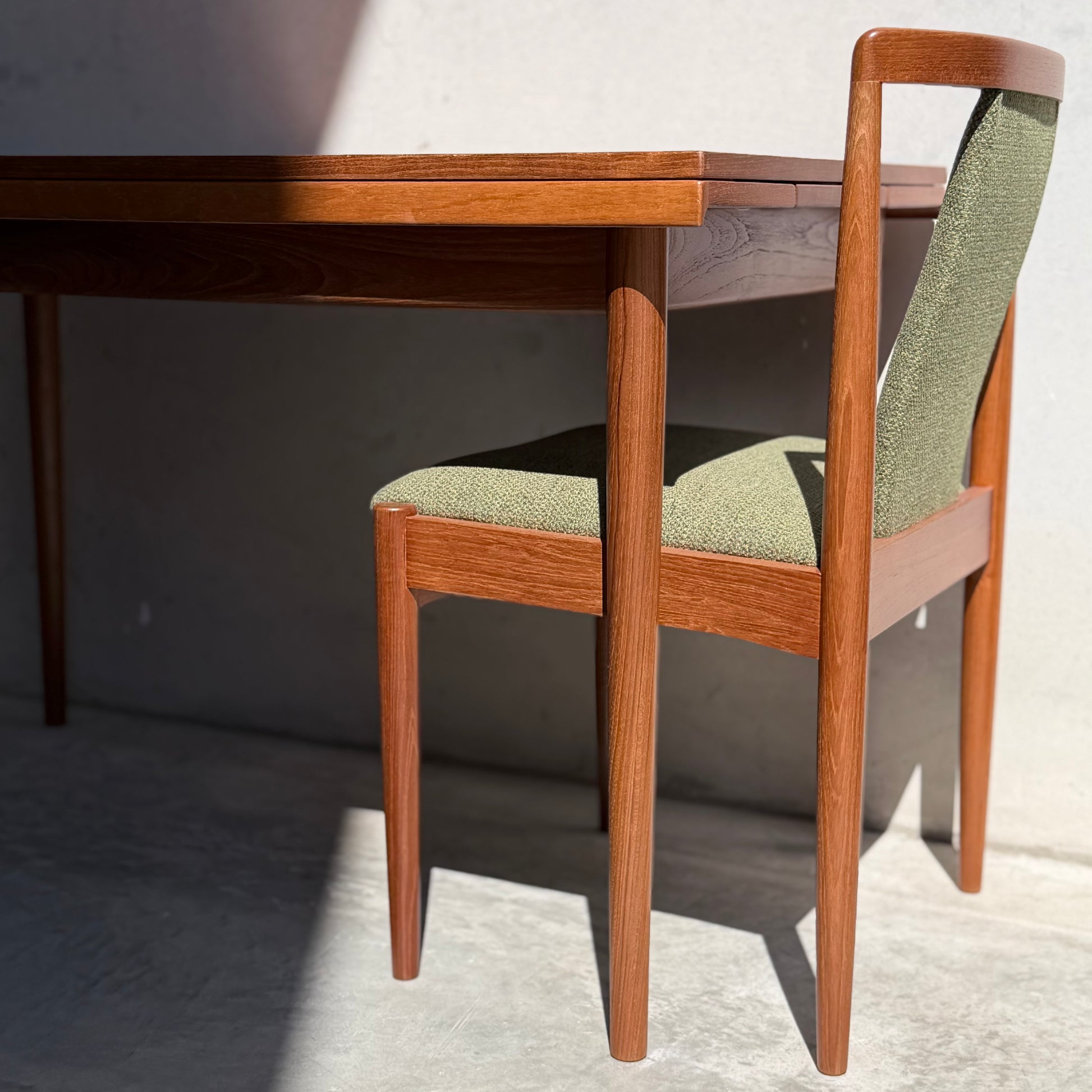 The Fully Restored Parker Dining Suite 5 Piece - Forest Green (Rediscover) features a mid-century wooden table and matching green-upholstered chair, bathed in sunlight on a concrete floor for a Scandinavian-inspired look.