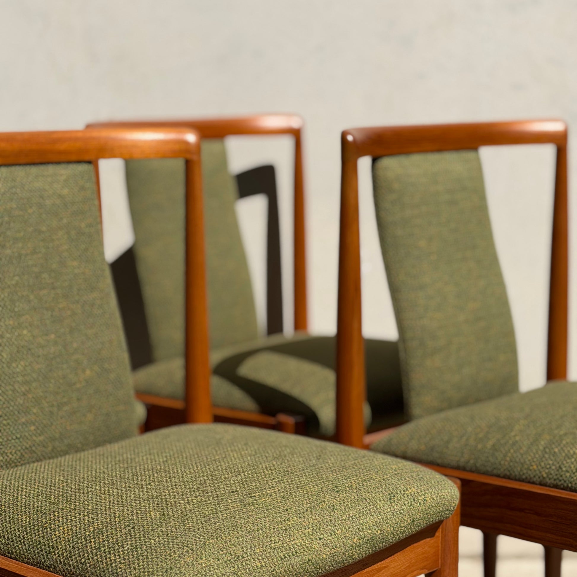 A set of four fully restored Parker T-Back Number 88 dining chairs in forest green (Rediscover) are grouped together, casting soft shadows on a light wall—a perfect showcase of mid-century modern style.