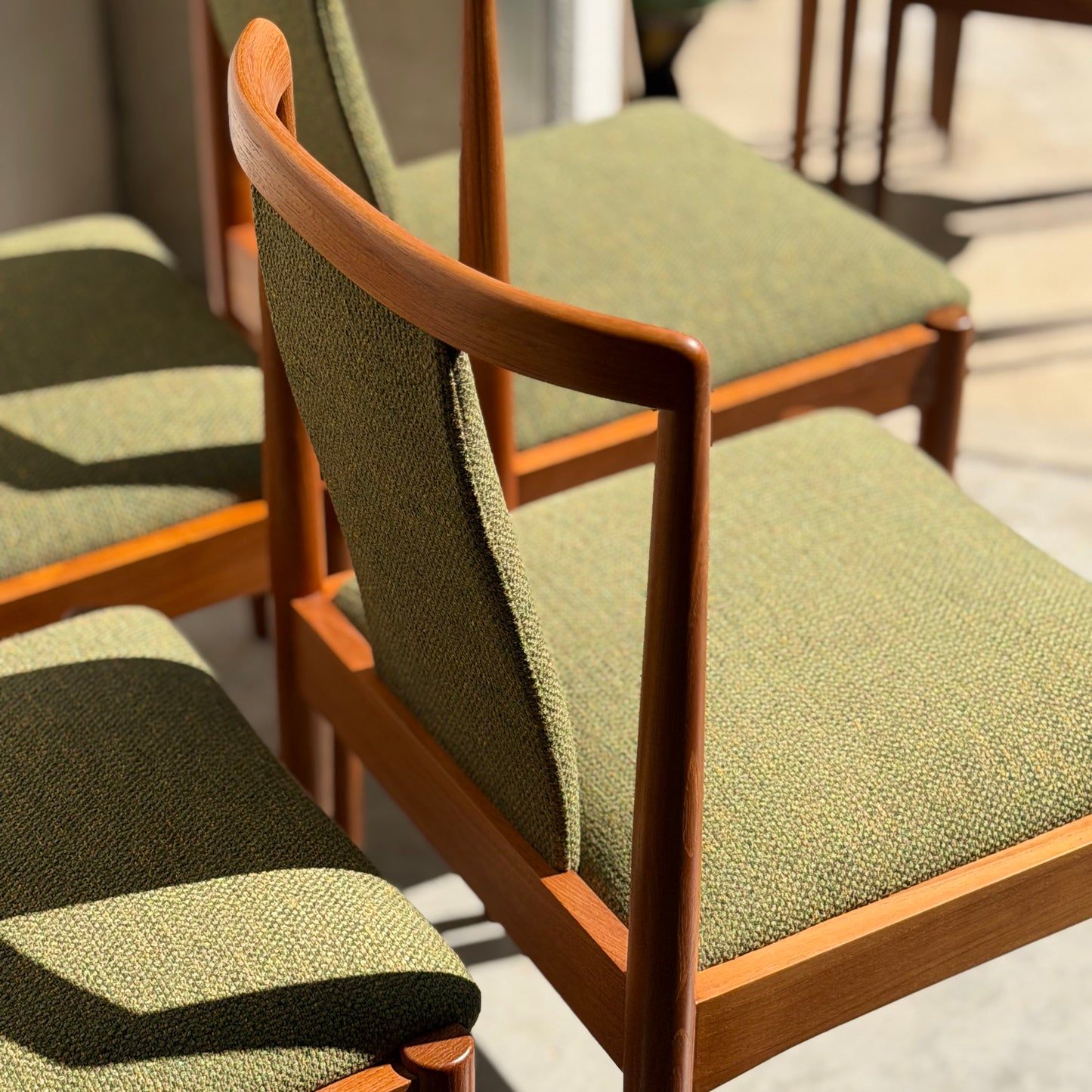 A set of four fully restored Parker T-Back Number 88 dining chairs in forest green from Rediscover are arranged in sunlight, showcasing their mid-century modern wooden frames and angled backs on a light-colored floor.