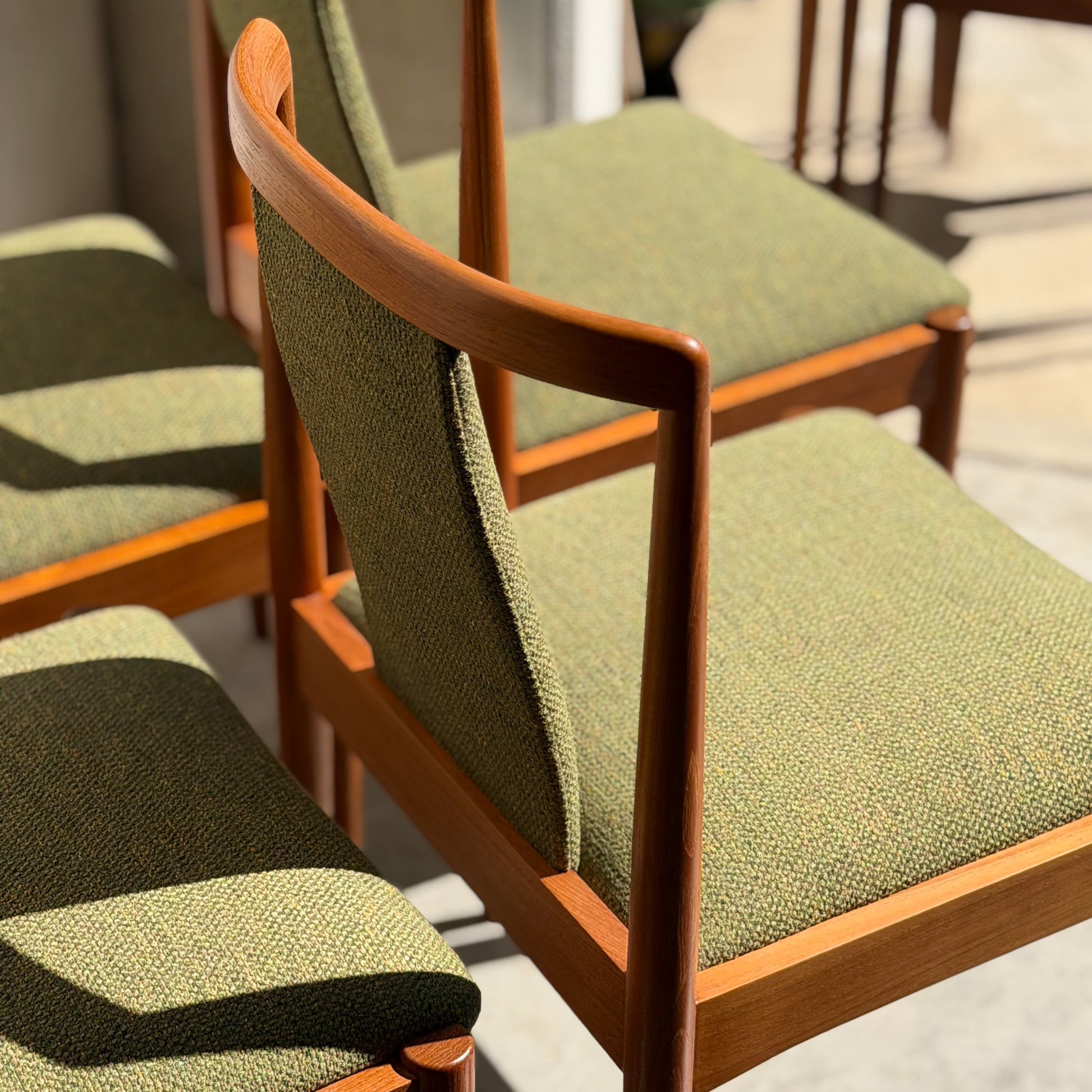 A set of four fully restored Parker T-Back Number 88 dining chairs in forest green from Rediscover are arranged in sunlight, showcasing their mid-century modern wooden frames and angled backs on a light-colored floor.