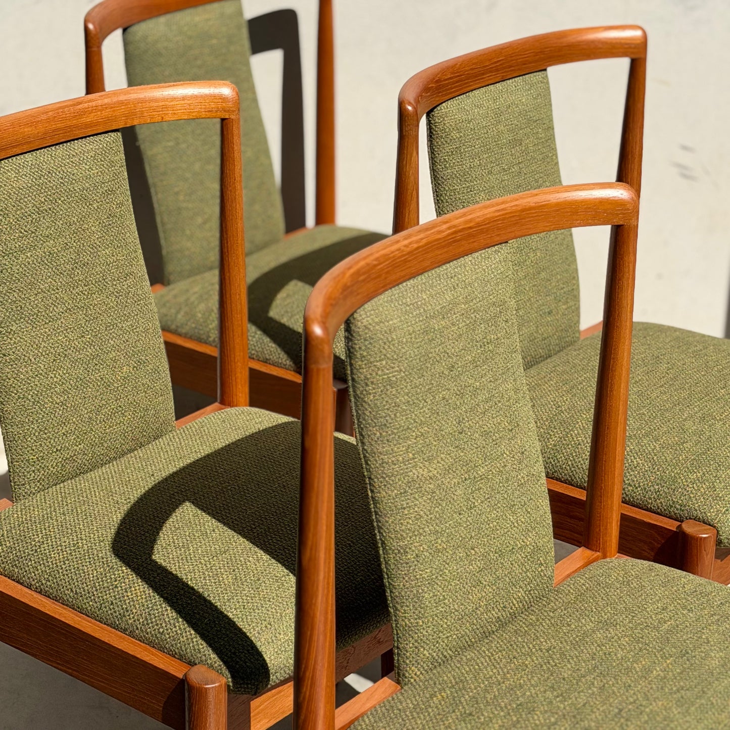 A set of four fully restored Parker T-Back Number 88 dining chairs in forest green (Rediscover) are arranged together, sunlight highlighting their mid-century modern frames and curved backrests.