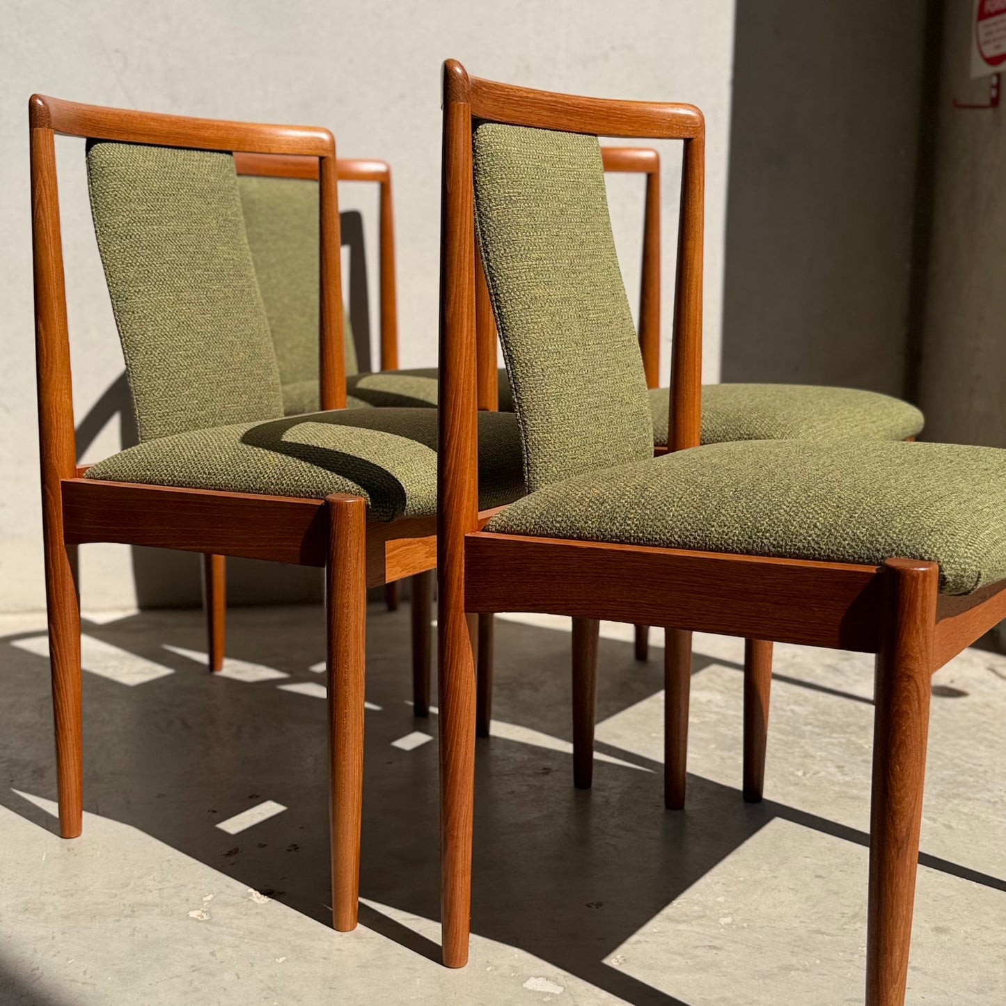 A set of four fully restored Parker T-Back Number 88 dining chairs in forest green from Rediscover are arranged on a sunlit concrete floor, casting distinct mid-century modern shadows.