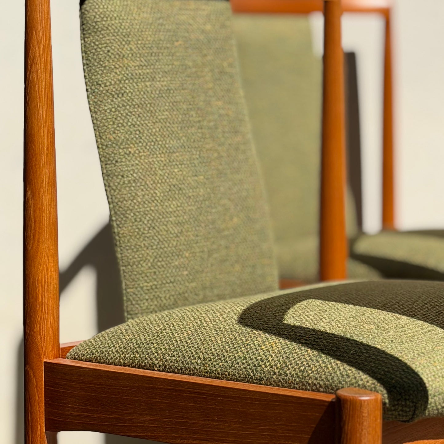 Close-up of two Fully Restored Parker T-Back Number 88 Dining Chairs from the Set of 4 – Forest Green (Rediscover), with textured seats and backrests in sunlight. The front teak chair is in sharp focus, the other softly blurred behind.