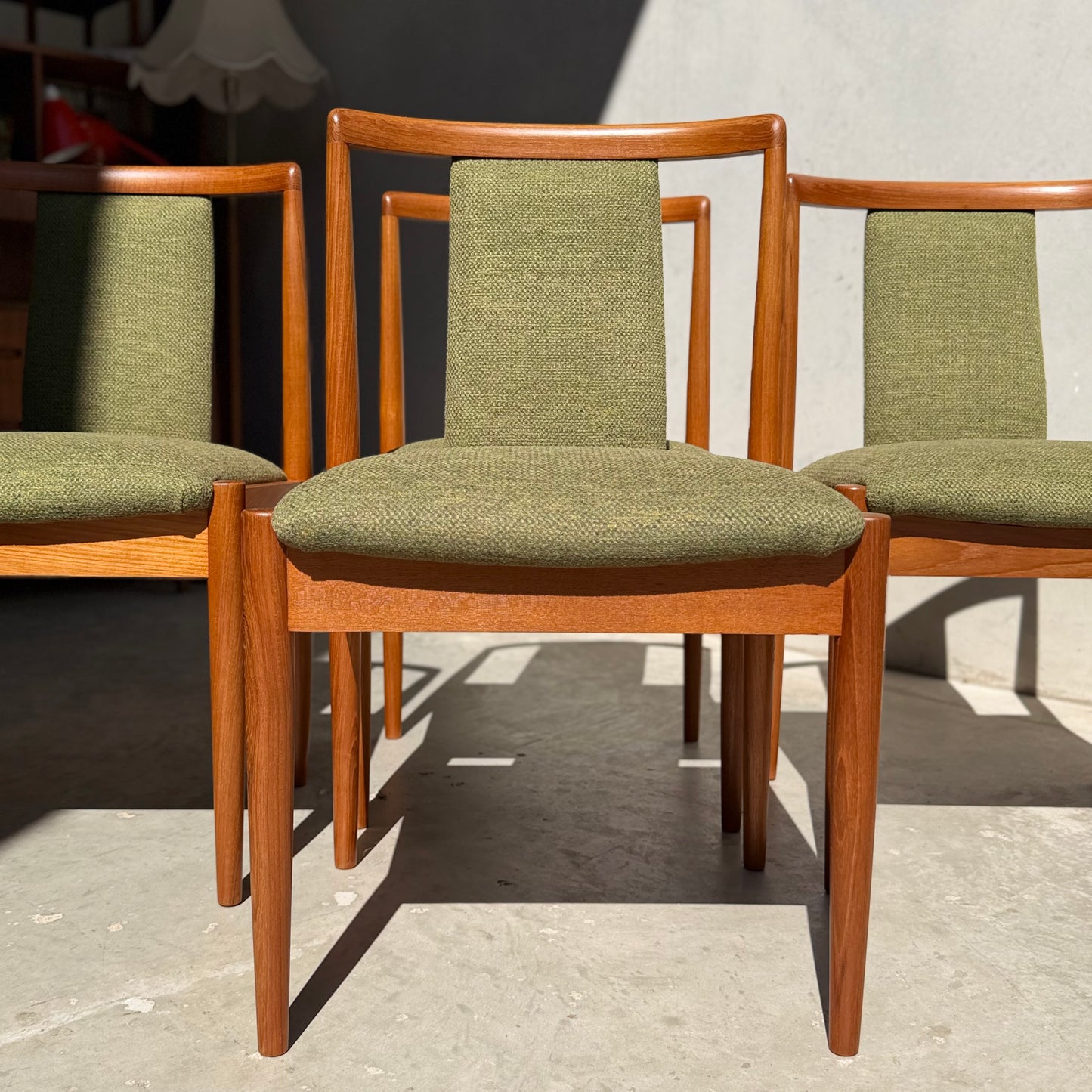 A set of four fully restored Parker T-Back Number 88 dining chairs in forest green (Rediscover) are arranged in sunlight by a light grey wall, highlighting their classic mid-century modern style.