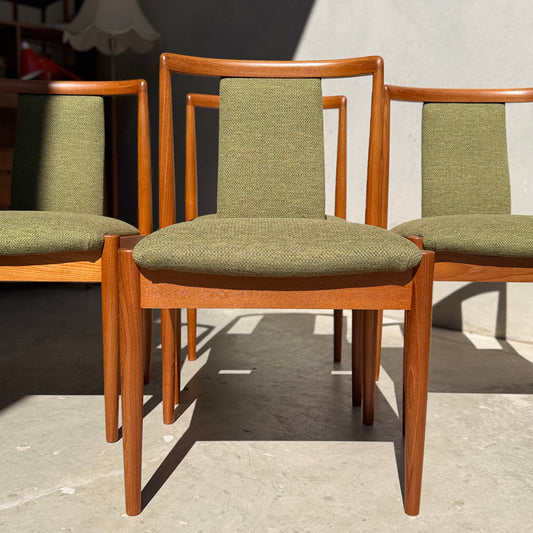 A set of four fully restored Parker T-Back Number 88 dining chairs in forest green (Rediscover) are arranged in sunlight by a light grey wall, highlighting their classic mid-century modern style.