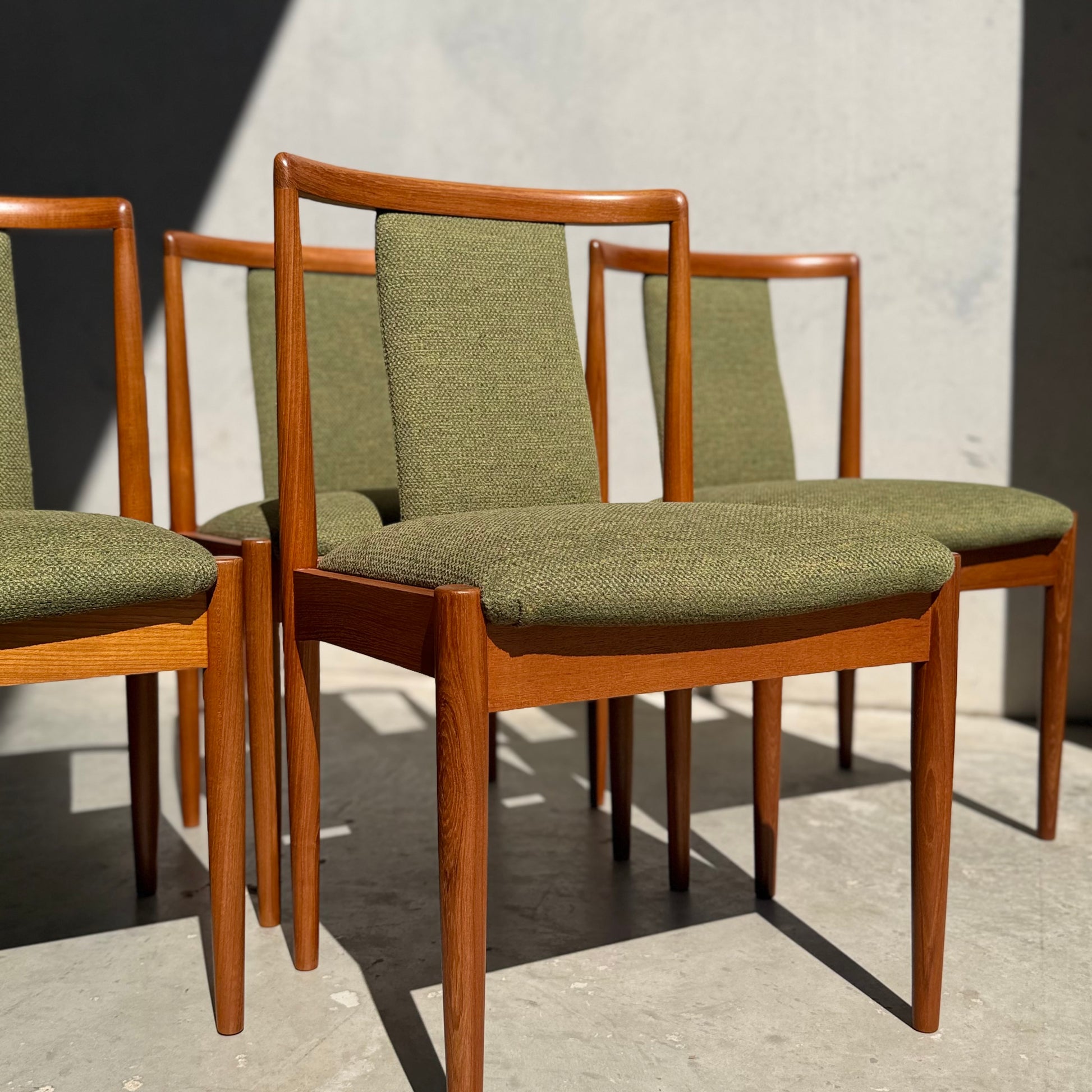 A set of four fully restored Parker T-Back Number 88 dining chairs in forest green (Rediscover) sits on a concrete floor, with sunlight casting shadows on the wall and floor behind them.