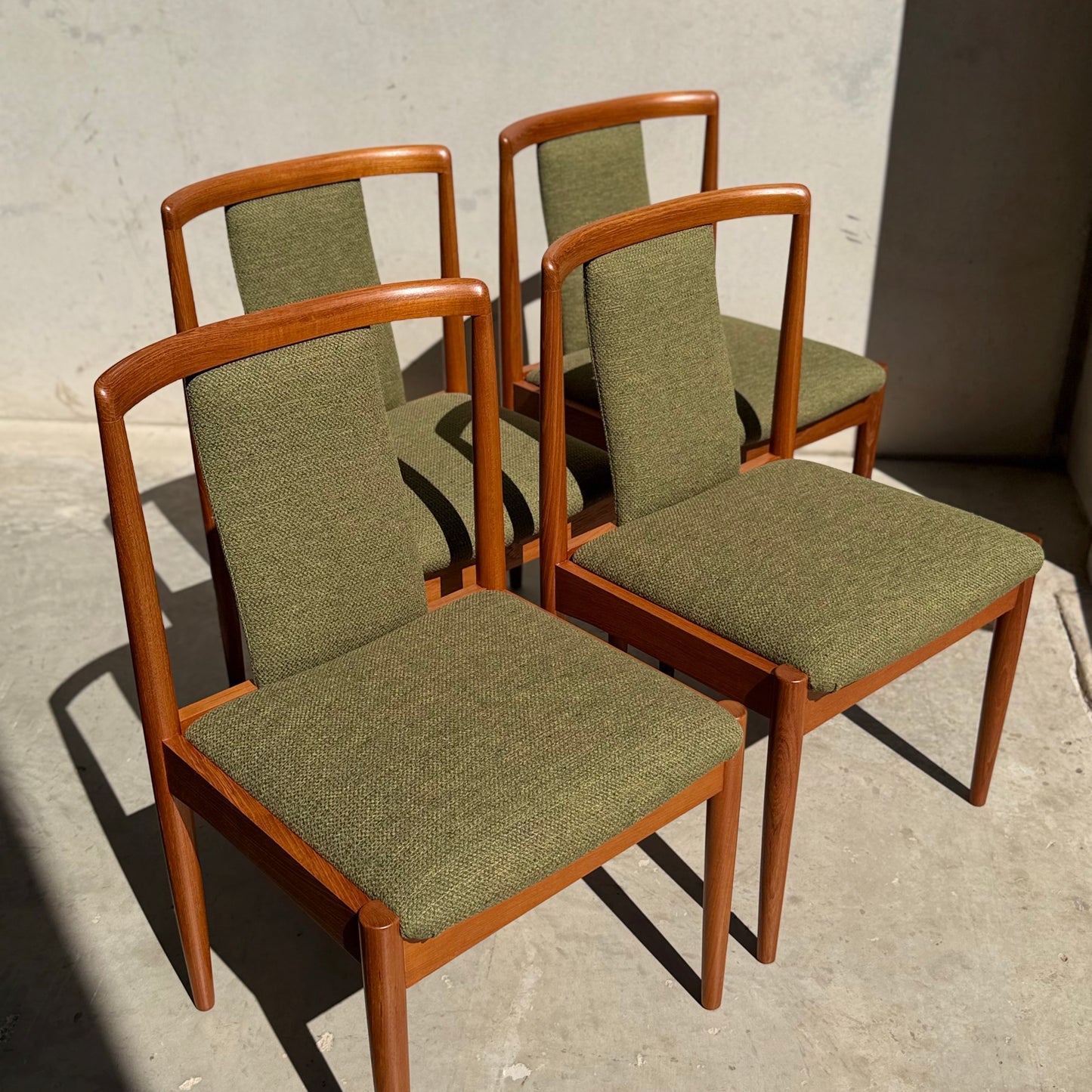 A set of four fully restored Parker T-Back Number 88 dining chairs in forest green (Rediscover) are arranged on a concrete floor, their crisp mid-century modern shadows cast in bright sunlight.