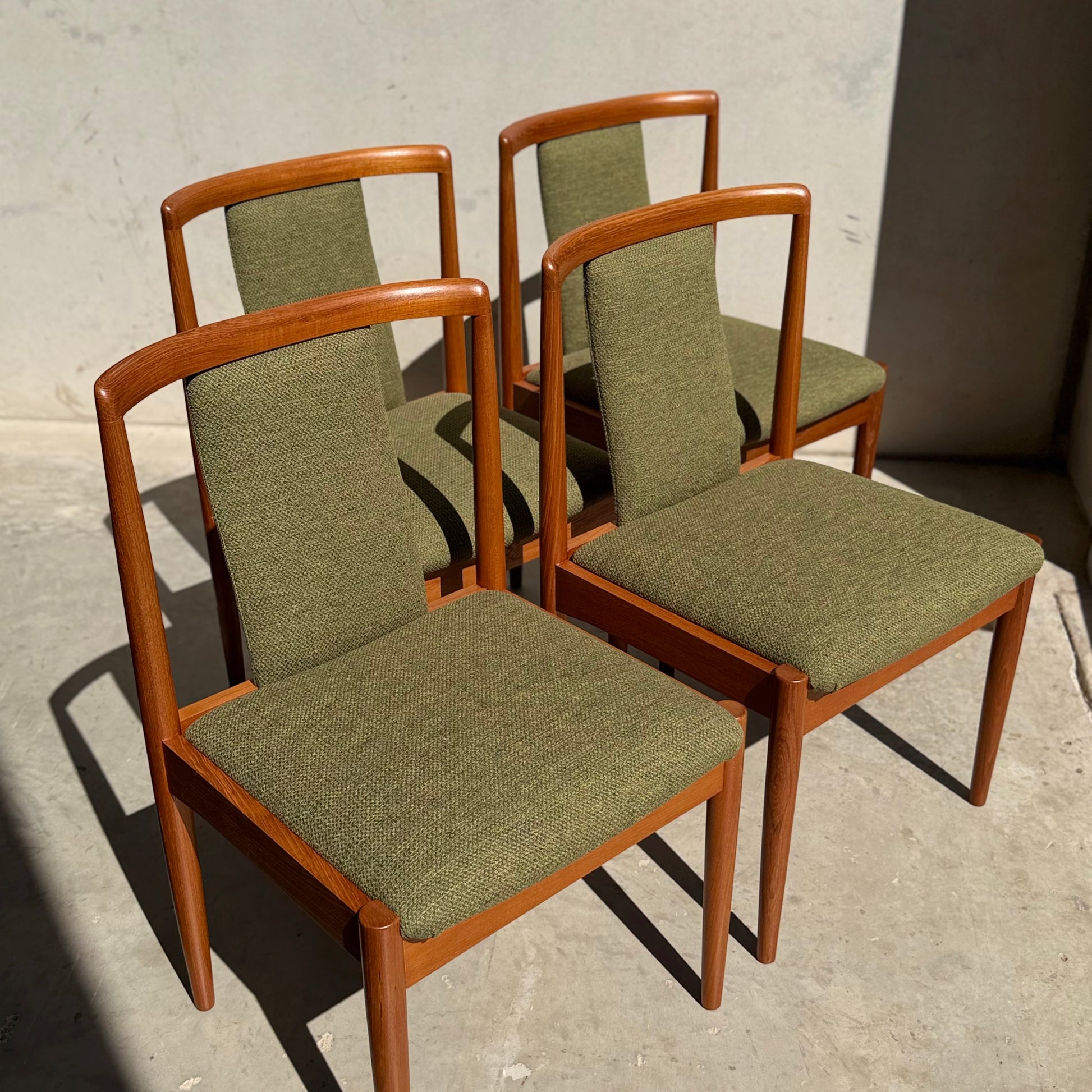 A set of four fully restored Parker T-Back Number 88 dining chairs in forest green (Rediscover) are arranged on a concrete floor, their crisp mid-century modern shadows cast in bright sunlight.
