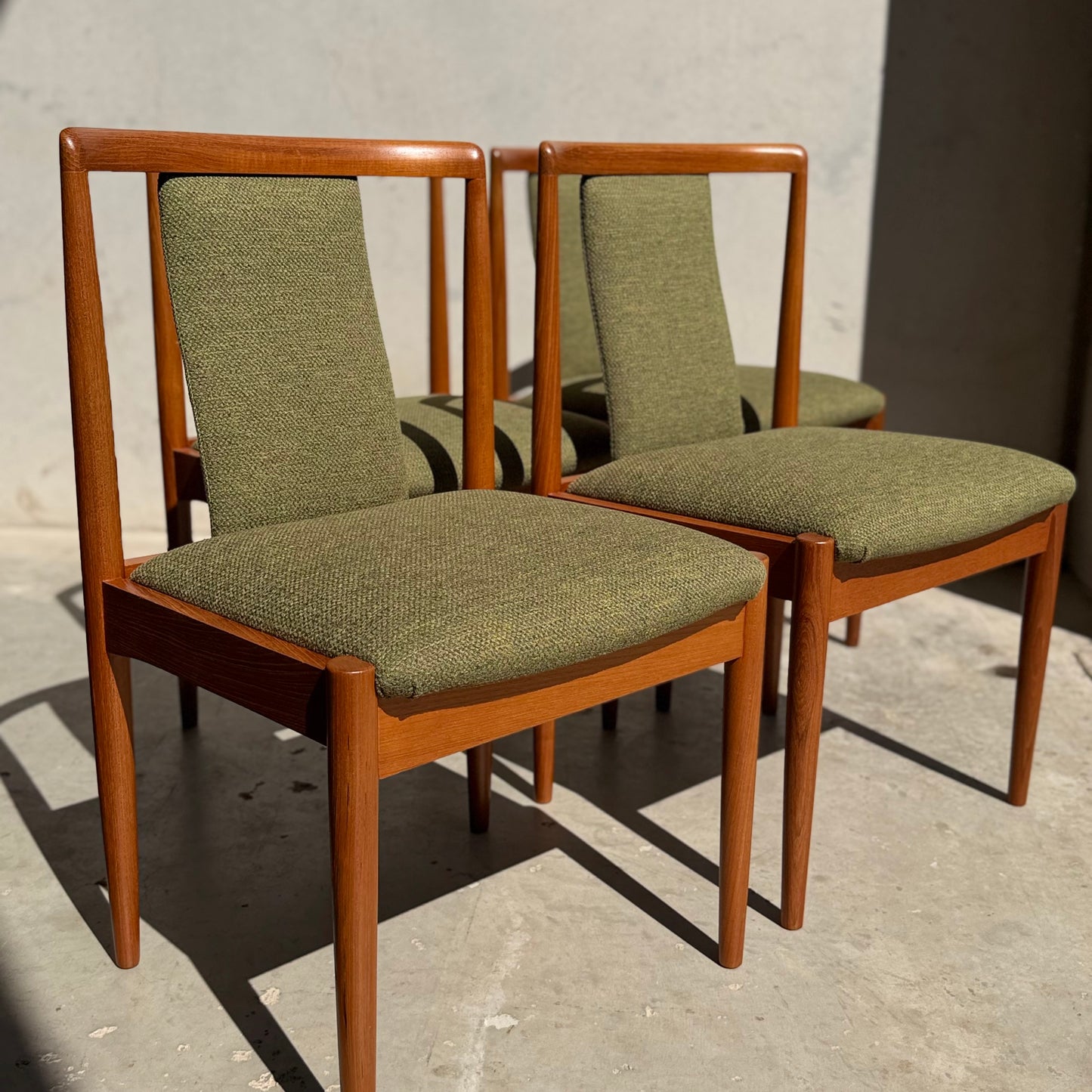 A set of four fully restored Parker T-Back Number 88 dining chairs in forest green (Rediscover) are arranged on a sunlit concrete floor, casting striking shadows and showcasing mid-century modern style.