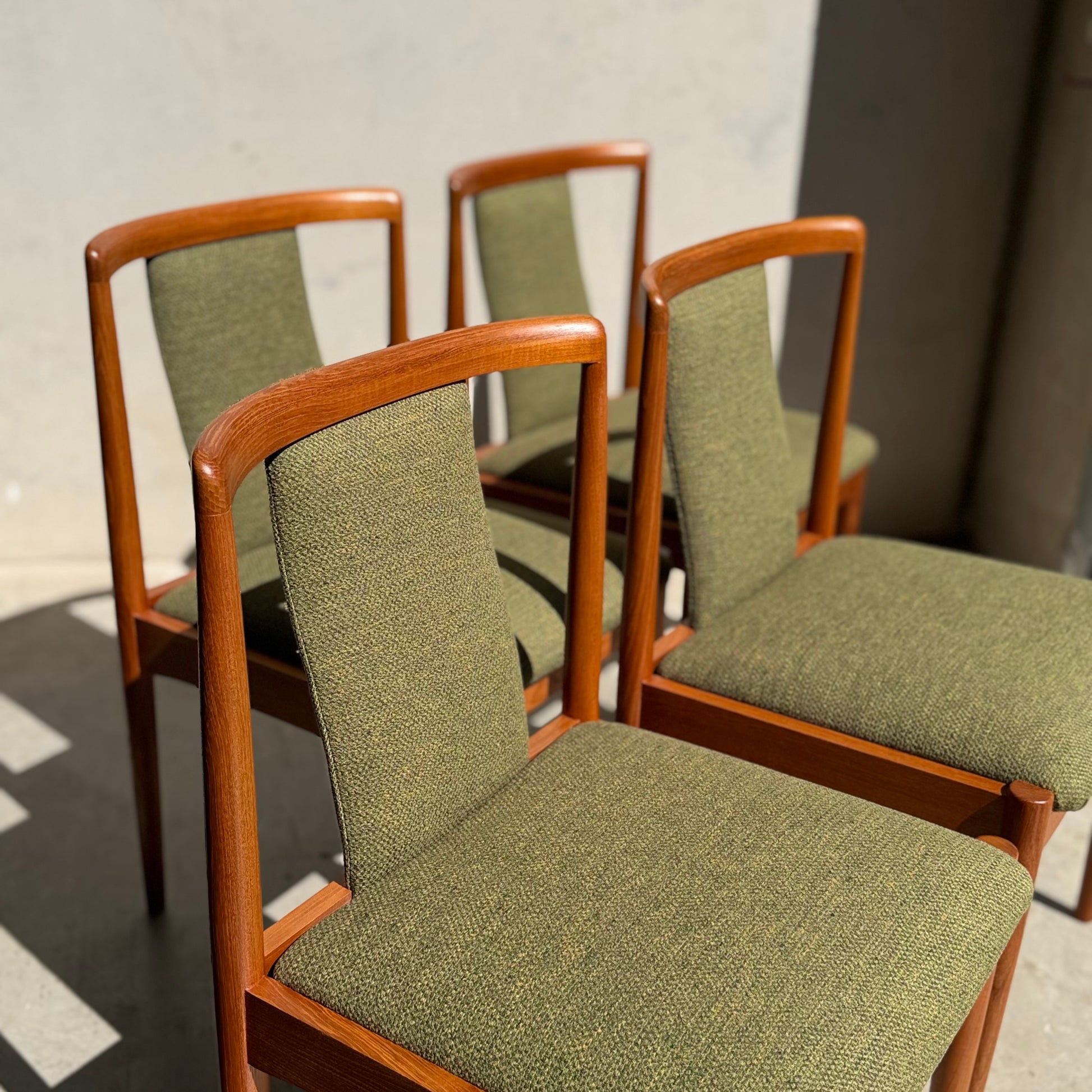 A set of four fully restored Parker T-Back Number 88 Dining Chairs in forest green upholstery is arranged in sunlight against a plain wall, casting soft shadows for a classic mid-century modern look.