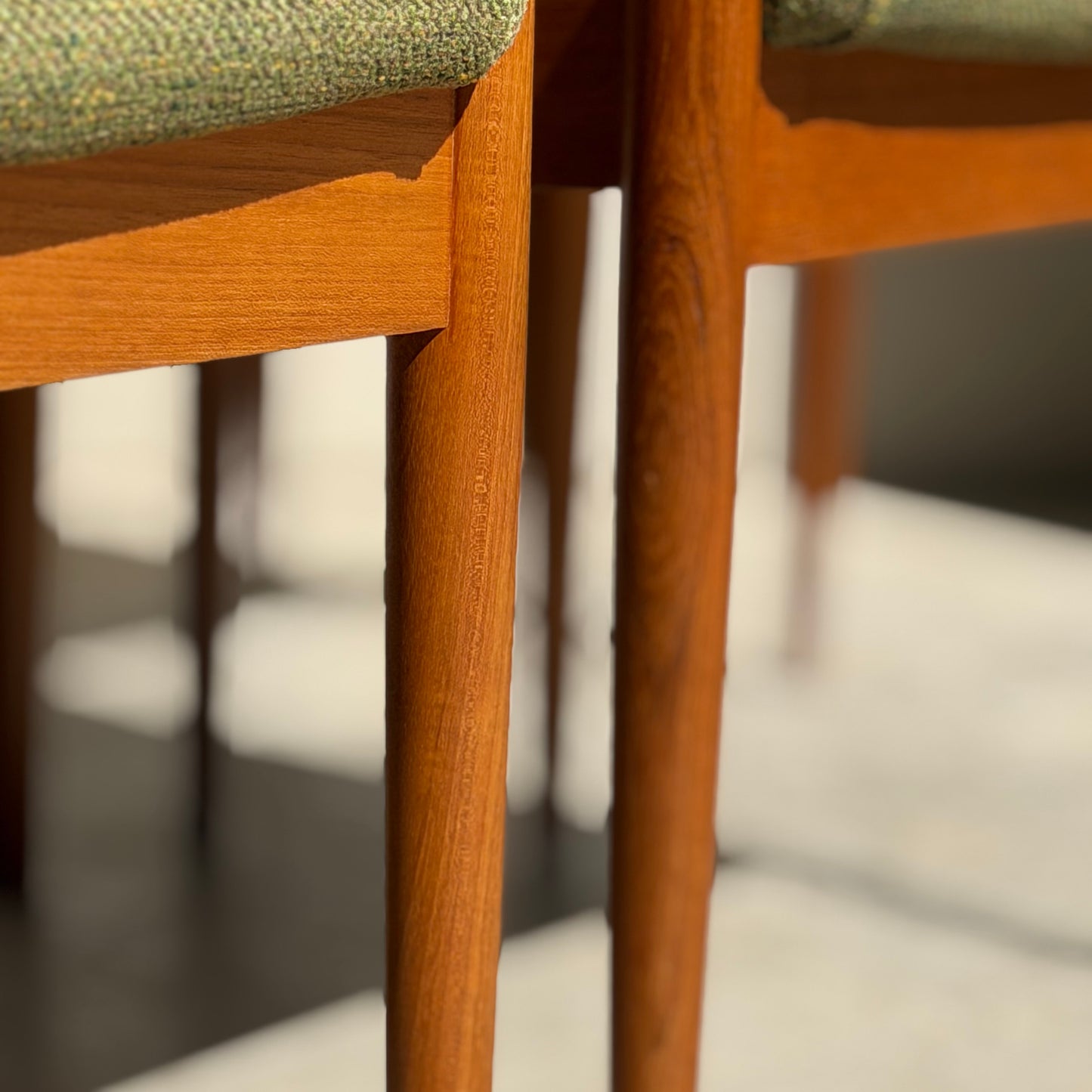 Close-up of the fully restored Parker T-Back Number 88 Dining Chairs Set of 4 - Forest Green (Rediscover), showcasing elegant wooden legs, green upholstery, and mid-century modern design in sunlight with soft floor shadows.