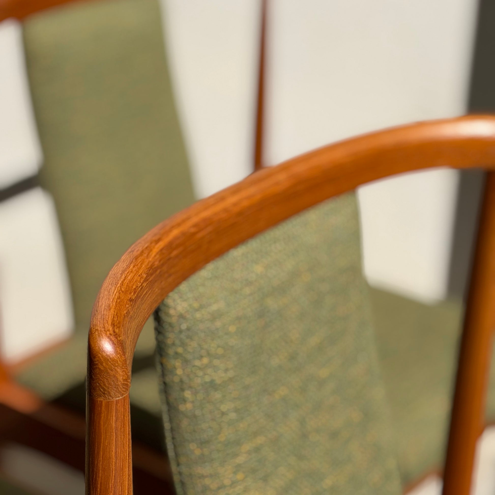 Close-up of a Fully Restored Parker T-Back Number 88 Dining Chair’s smooth wooden armrest and forest green cushion from the Set of 4. Another teak chair sits blurred in the background, both reflecting timeless mid-century modern style.