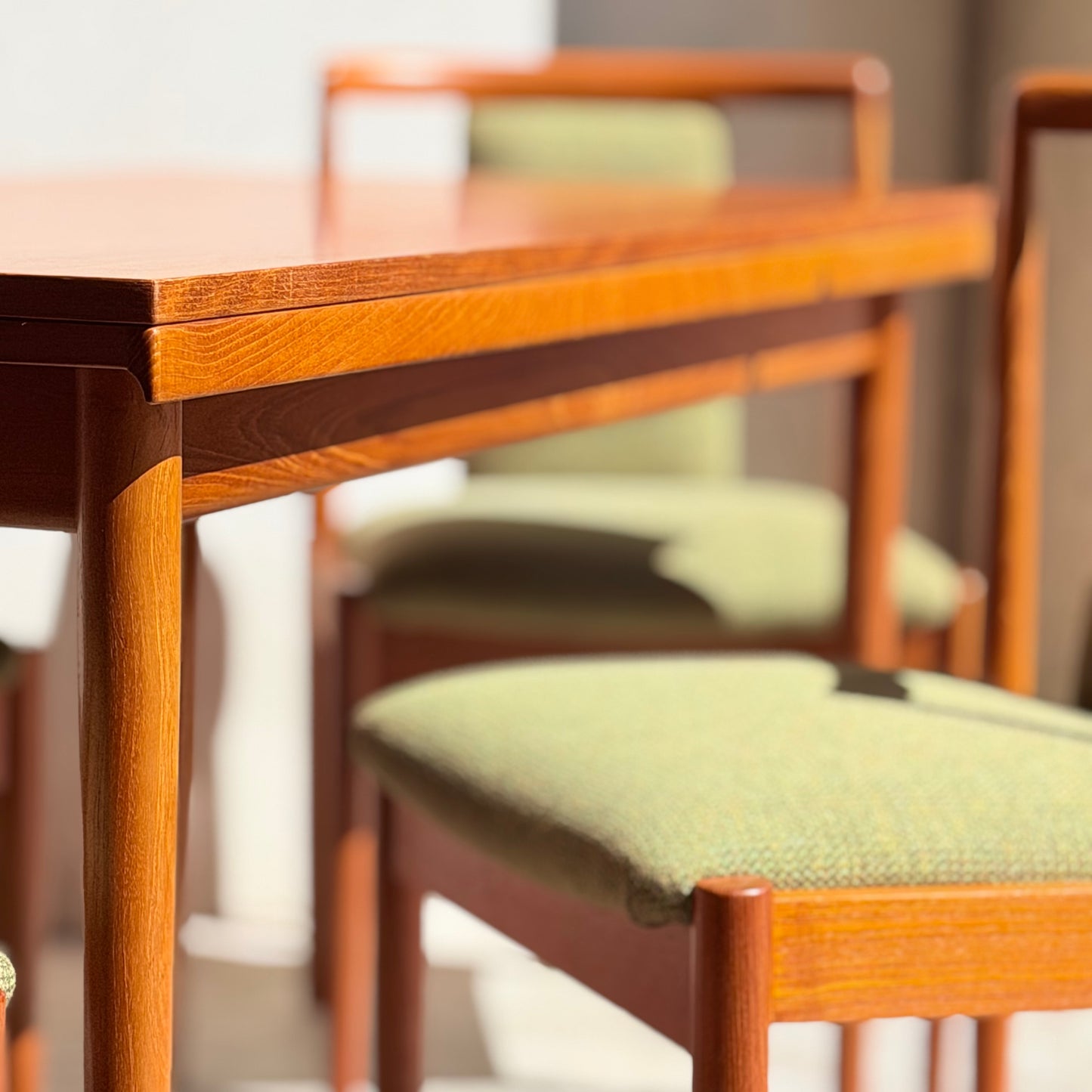 A close-up of the Fully Restored Parker Dining Suite 5 Piece - Forest Green (Rediscover) shows wooden table and chairs with forest green seats, bathed in sunlight, highlighting its Scandinavian-inspired design.
