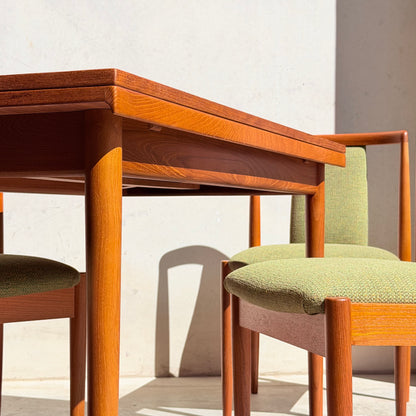 A close-up of the Fully Restored Parker Dining Suite 5 Piece—Forest Green by Rediscover, showcasing two wooden chairs with green upholstered seats and a matching table in sunlight against a light wall for mid-century modern style.