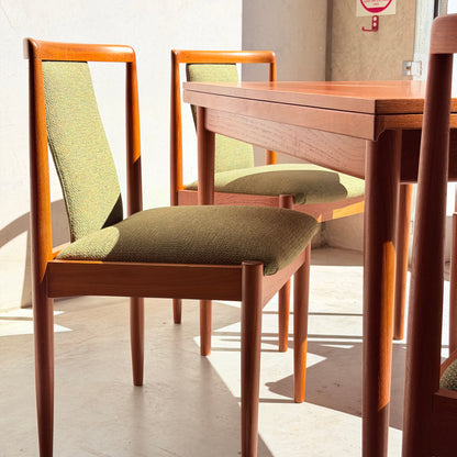 Two wooden chairs with green fabric seats and backs from the Fully Restored Parker Dining Suite 5 Piece – Forest Green (Rediscover) sit by a wooden table in bright sunlight, casting clear shadows on a light-colored floor.