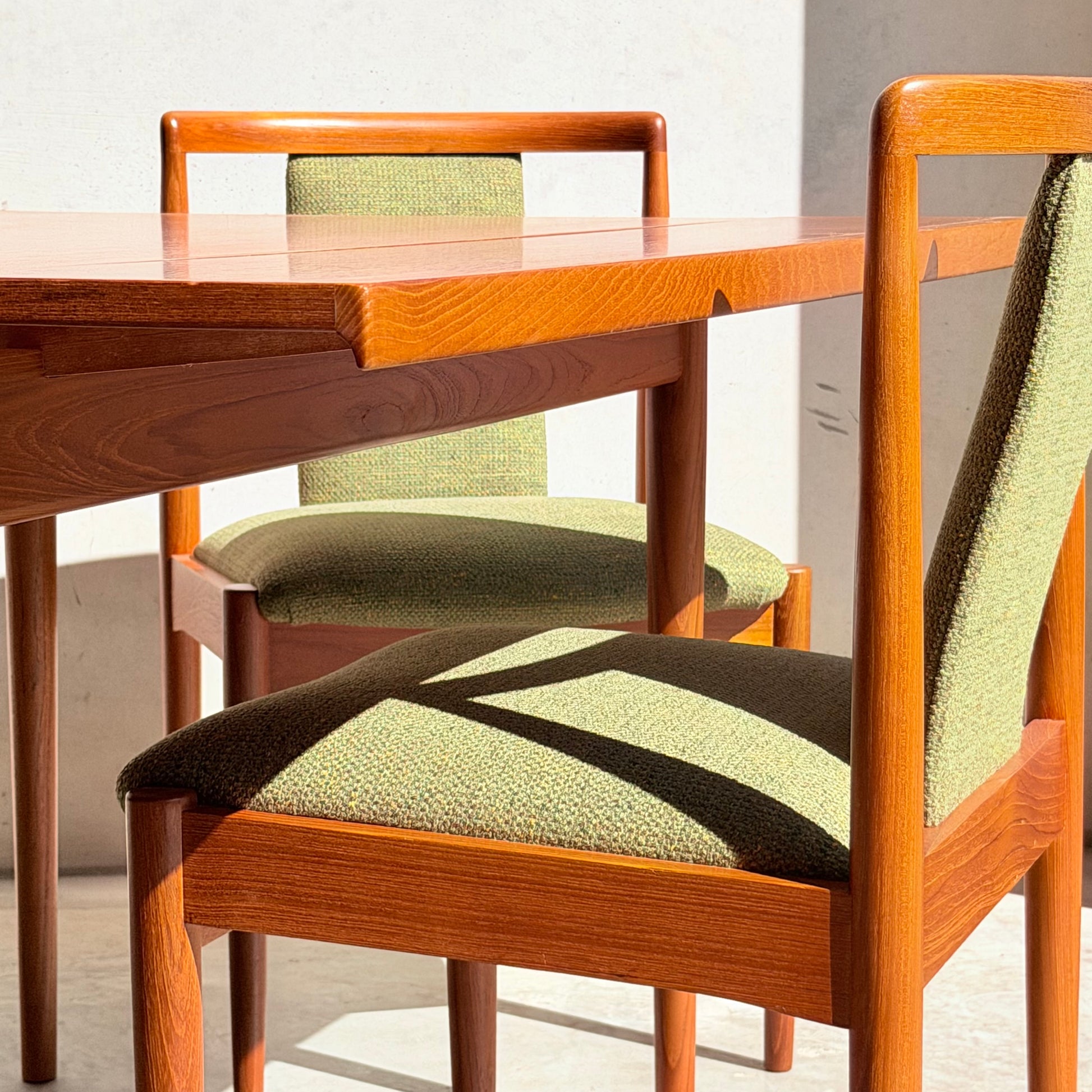 The Fully Restored Parker Dining Suite 5 Piece – Forest Green features two wooden chairs with green upholstery at a matching table, creating a Scandinavian mid-century modern dining set bathed in sunlight with distinct floor shadows.