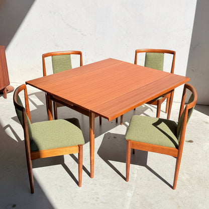 Featuring four forest green upholstered chairs, the Fully Restored Parker Dining Suite 5 Piece (Rediscover) showcases a square wooden table with a reddish-brown finish, set on a light concrete floor dappled with sunlight.