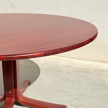 The Joe Rufenacht Designer Round Dining Table – Rare Mid-Century Gem in Solid Wood (Refine) features a polished, reddish-brown finish and mid-century modern style, shown on a concrete floor with a plain light-colored wall backdrop.