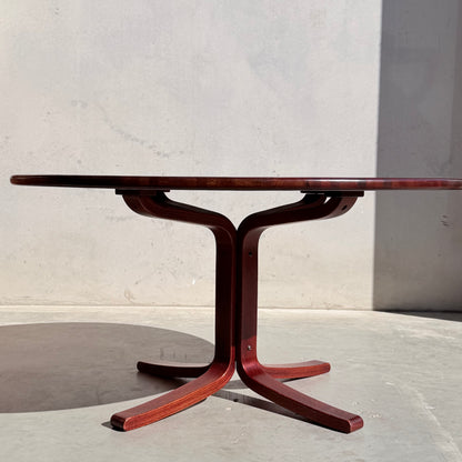The Joe Rufenacht Designer Round Dining Table – Rare Mid-Century Gem in Solid Wood (Refine) features a reddish-brown pedestal base and stands on a concrete floor, its shadow falling against a plain, light-colored wall.