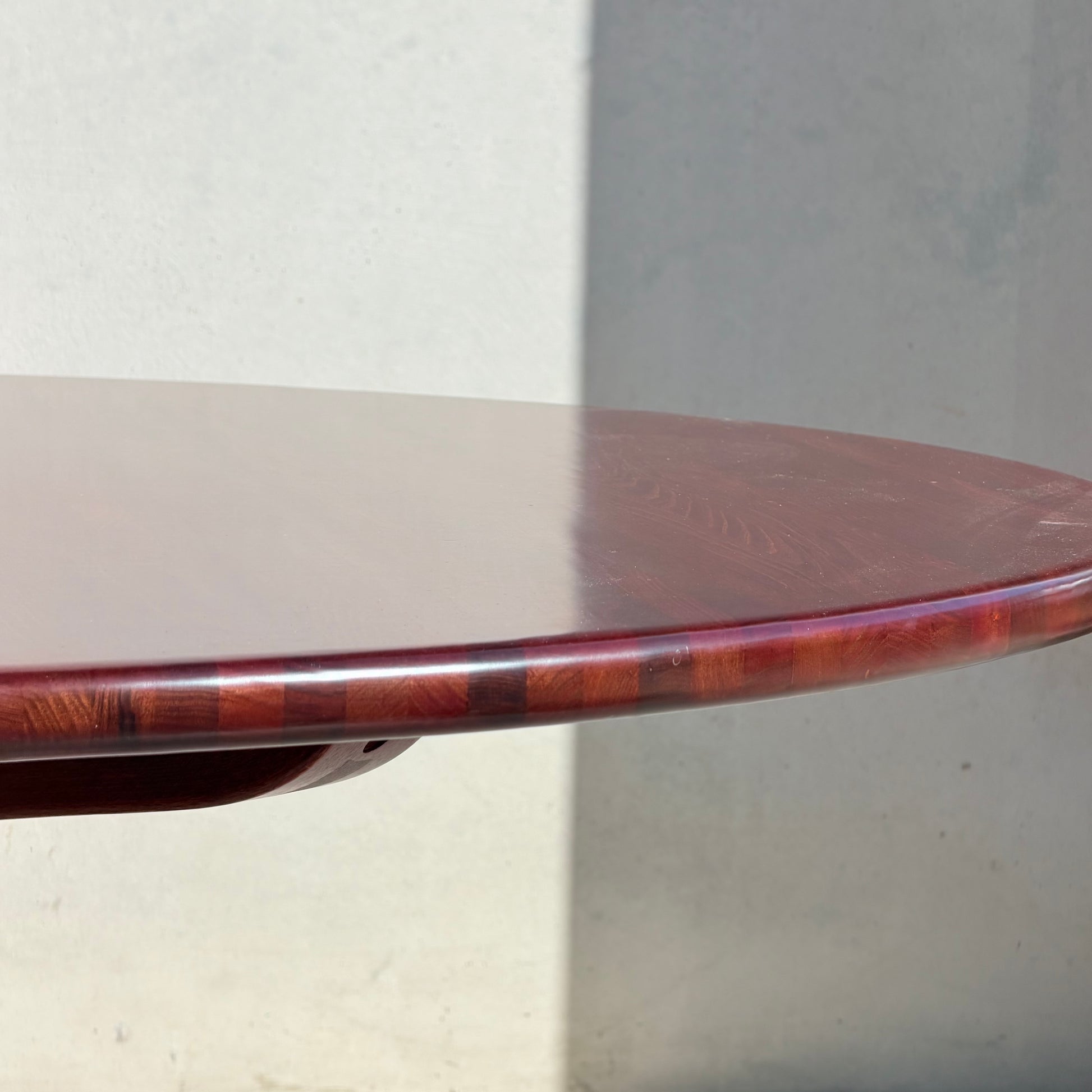 Close-up of the Joe Rufenacht Designer Round Dining Table – Rare Mid-Century Gem in Solid Wood (Refine), showcasing its polished reddish-brown finish and elegant edge, set against a plain light wall with a subtle shadow.