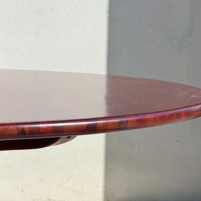 Close-up of the Joe Rufenacht Designer Round Dining Table – Rare Mid-Century Gem in Solid Wood (Refine), showcasing its polished reddish-brown finish and elegant edge, set against a plain light wall with a subtle shadow.