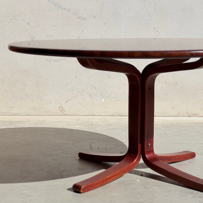 The Joe Rufenacht Designer Round Dining Table – Rare Mid-Century Gem in Solid Wood casts a shadow on a concrete floor, set against a plain, light wall, highlighting its refined curved legs and designer appeal.