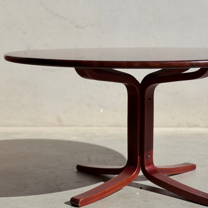 The Joe Rufenacht Designer Round Dining Table – Rare Mid-Century Gem in Solid Wood (Refine) features a polished surface and sculpted pedestal base, casting a shadow on a light gray floor against a plain, light-colored wall.
