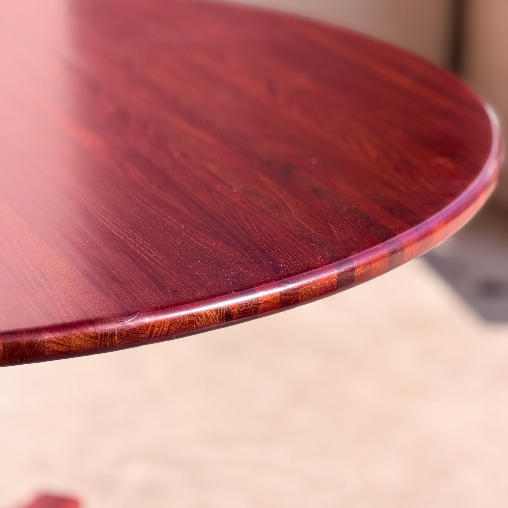 A close-up of the Joe Rufenacht Designer Round Dining Table—rare mid-century gem in solid wood—shows its polished, reddish-brown finish and rich wood grain, highlighting its smooth, glossy surface.