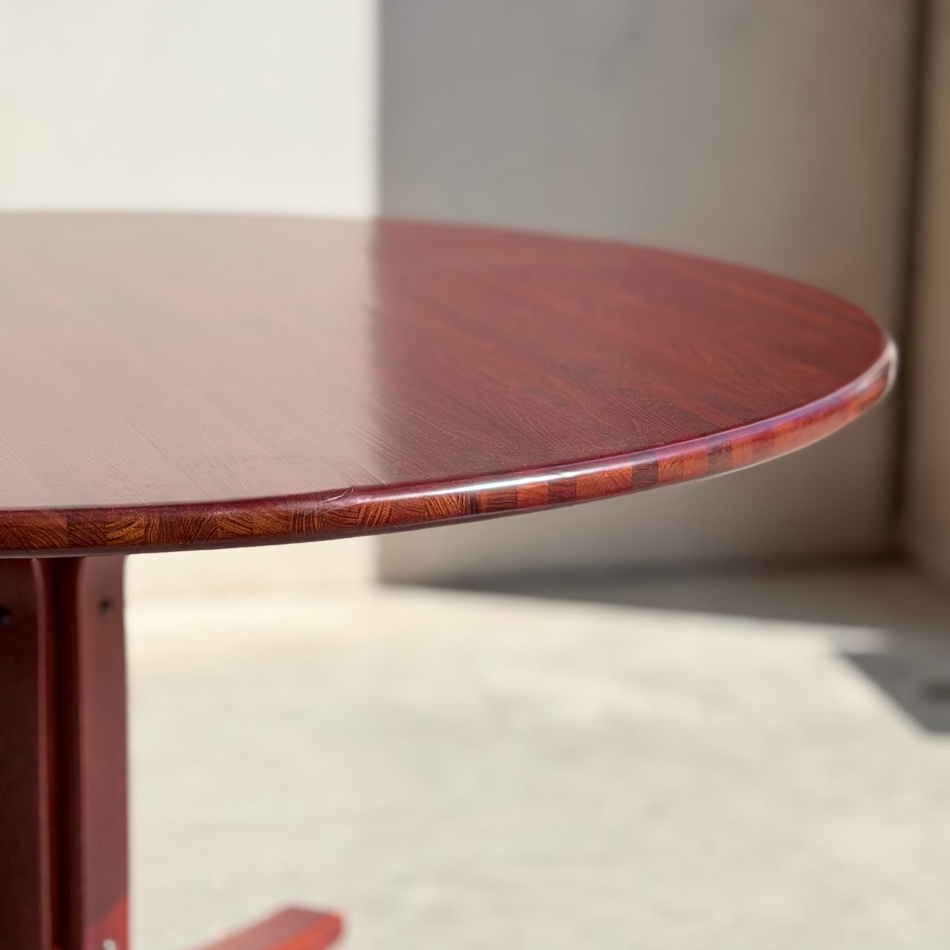A close-up of the Joe Rufenacht Designer Round Dining Table – a rare mid-century gem in solid wood, showcasing its polished reddish-brown surface in bright natural light against a plain, light background.