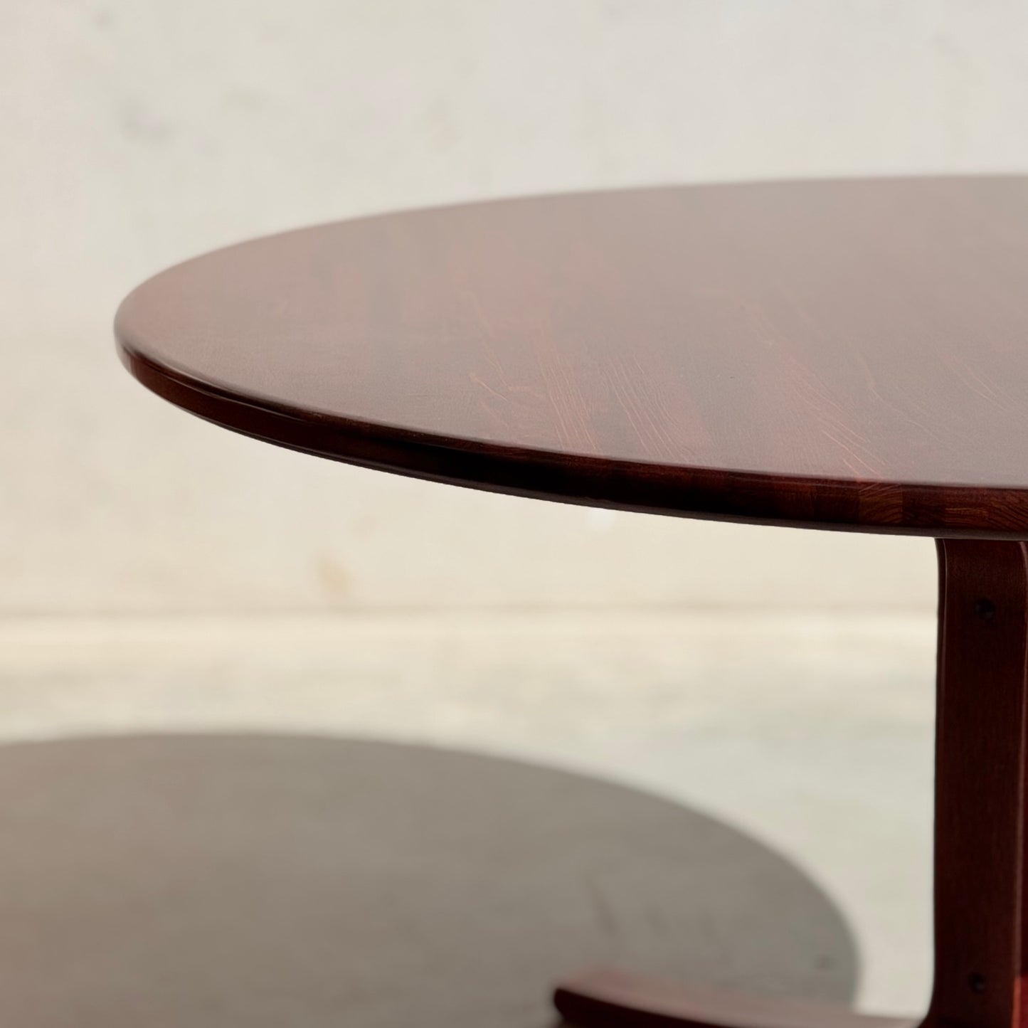 A close-up of the Joe Rufenacht Designer Round Dining Table – a rare mid-century solid wood gem with a dark brown finish, set against a light wall and casting a gentle shadow on the floor.