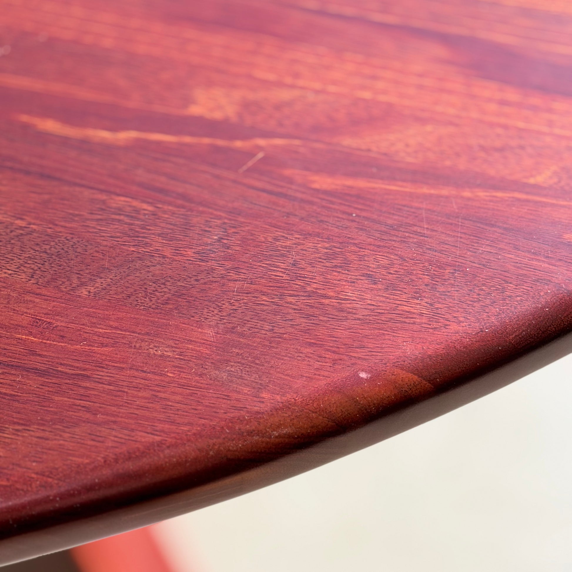 Close-up of the Joe Rufenacht Designer Round Dining Table—solid wood with a smooth, reddish-brown finish, visible grain, rounded edge, and subtle scratches; a rare mid-century modern gem highlighting natural texture.