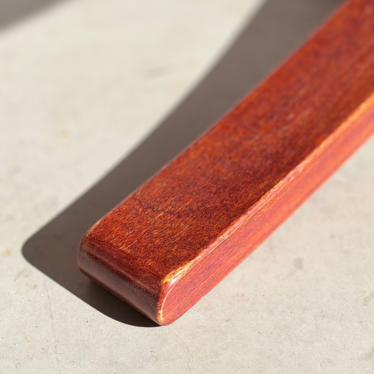 A polished, reddish-brown solid wood plank with rounded edges rests on a light surface, reflecting the craftsmanship of the Joe Rufenacht Designer Round Dining Table – Rare Mid-Century Gem in Solid Wood (Refine).