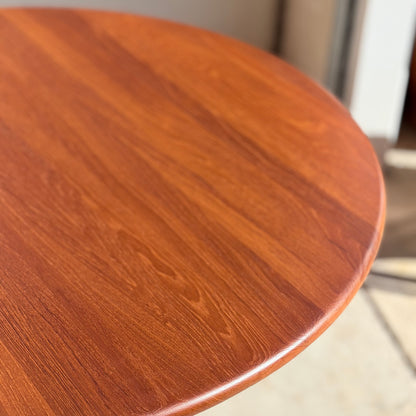 A close-up of the Fully Restored Solid Teak Danish Dining Table (Rediscover) showcases its smooth, polished surface and striking wood grain illuminated by natural light near a doorway.