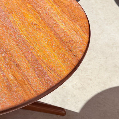 A close-up of the Fully Restored Solid Teak Danish Dining Table (Rediscover) shows its smooth, polished round surface with visible wood grain, casting a soft shadow on a light floor.