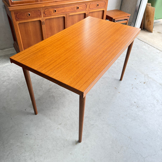 A Fully Restored Parker 95 Teak Nordic Extension Table (Rediscover) with a smooth, light brown finish and tapered legs stands on a concrete floor, accompanied by a matching sideboard and small table in the background.
