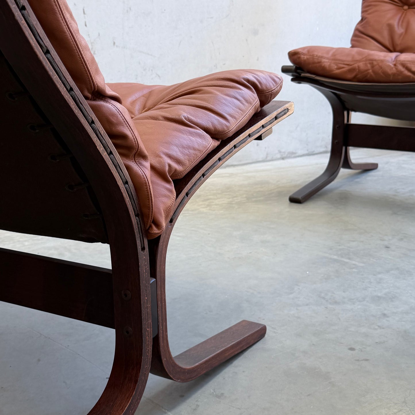 Close-up of the Signature Vintage Ingmar Relling Siesta Set—two lounge chairs with curved wooden frames and brown leather cushions, plus a rare coffee table—displayed on a light concrete floor against a plain white wall.