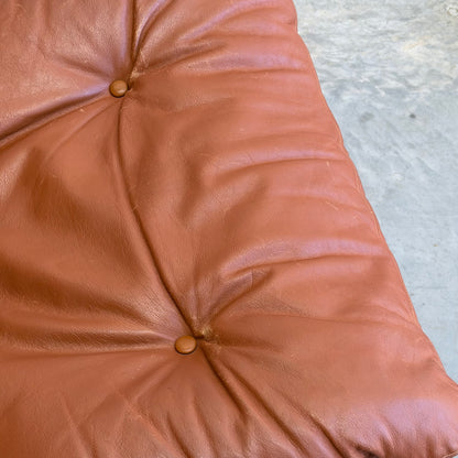 Close-up of a tufted brown leather cushion with two buttons from the Signature Vintage Ingmar Relling Siesta Set—Two Lounge Chairs & Rare Coffee Table—resting on a gray, textured concrete surface.